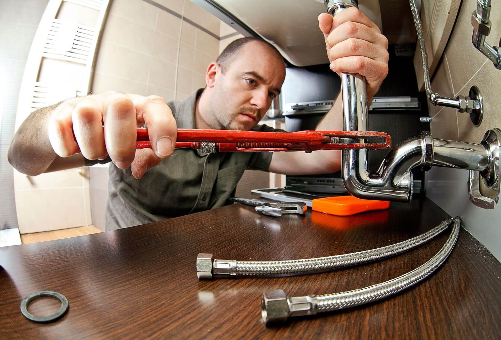 Plumber tightening a pipe fitting under a sink
